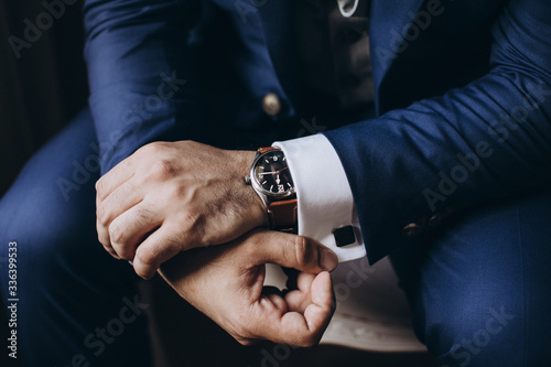 Man in a suit and a white shirt with a clock on his hands straightens the cuffs and cufflink