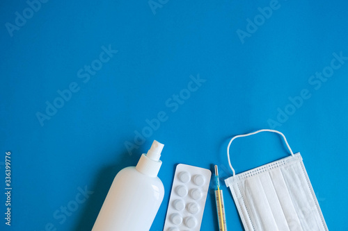 A set of medical disposable mask, antiseptic, pills and a mercury thermometer on a blue background. Medical hygiene and virus protection concept. Top view. Copy, empty space for text