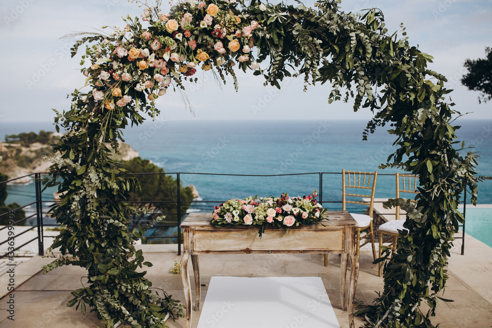 Fototapeta premium Wedding decorations. The ceremony area in the villa by the pool overlooking the sea is decorated with flower arrangements, golden vases and candles