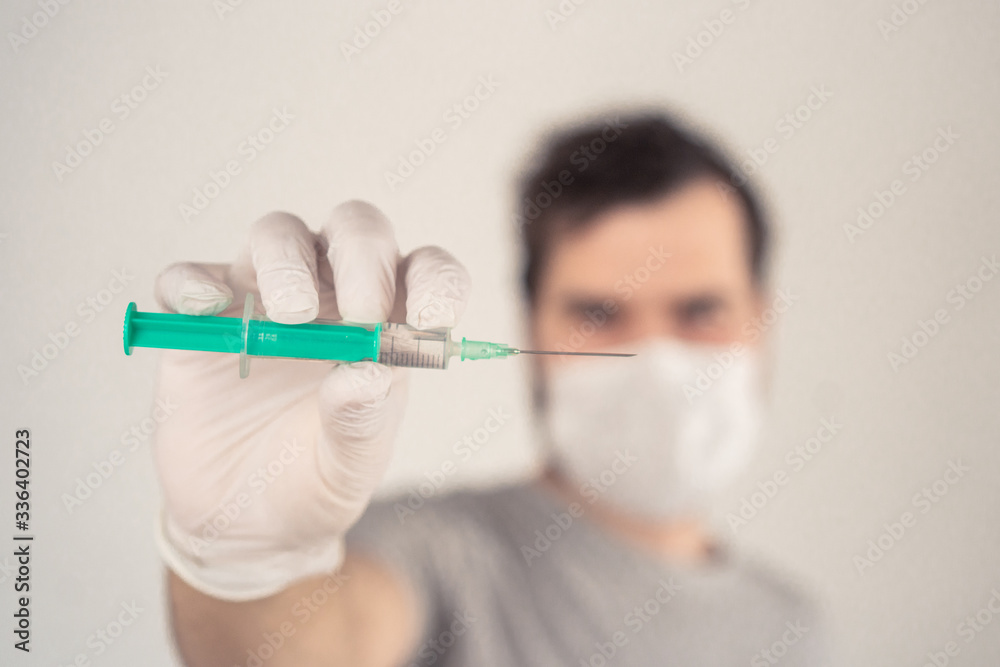 man in a medical mask with a syringe in his hands on a light background man in a medical mask with a syringe in his hands on a light background