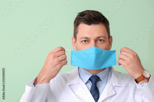 Doctor putting on protective medical mask against color background photo