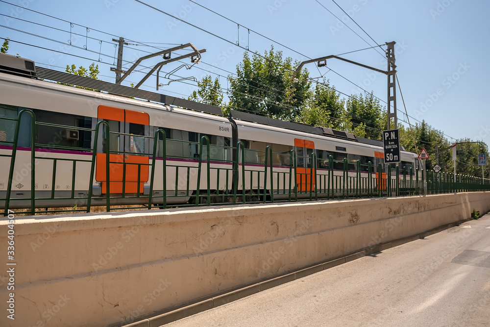 An electric train with multi-colored doors moves between a special fence along the road for wheeled vehicles.