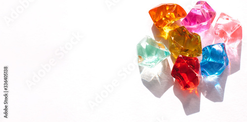 Bright multicolored transparent glass stones with the glare of the sun on a white background close up.Creative background,abstract texture.Copy space for text