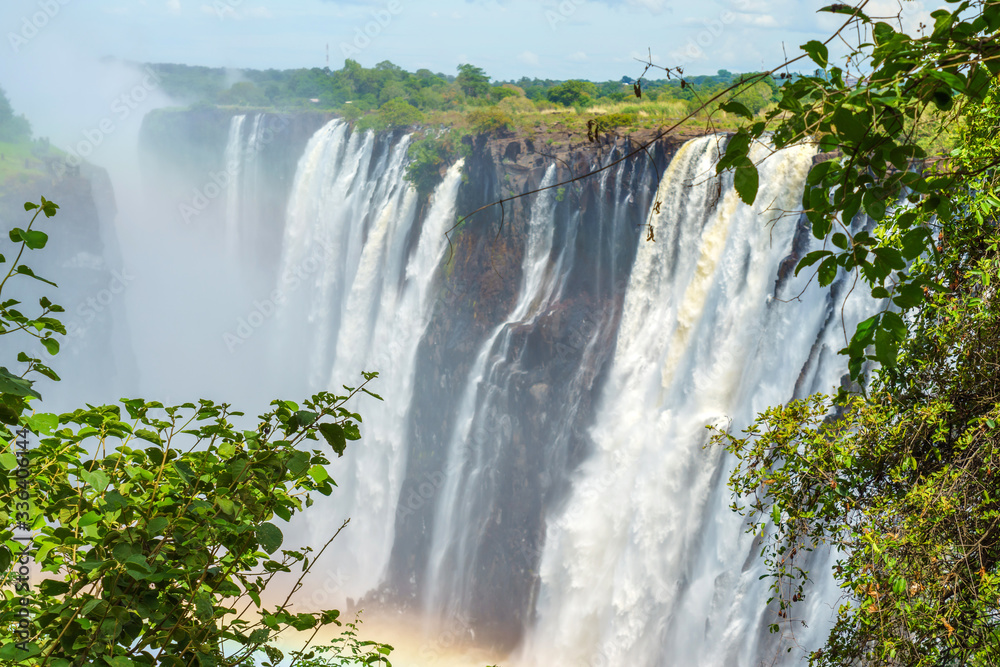 Panorama view with dramatic waterfall, rainbow and clouds at Victoria Falls, Zimbabwe, Zambia.