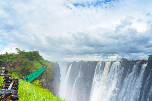Fototapeta Naklejka Na Ścianę i Meble -  Walking way with view to the dramatic waterfall and clouds at Victoria Falls on the Zambezi River, Zimbabwe, Zambia.