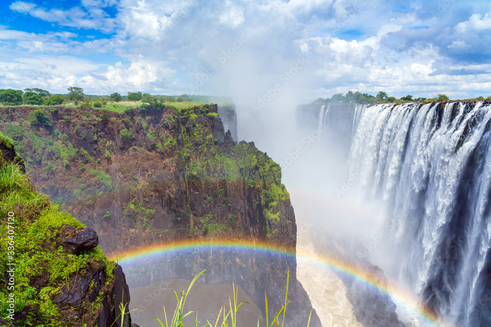 Panorama view with dramatic clouds and waterfall  with a rainbow at Victoria Falls on the Zambezi River, Zimbabwe, Zambia. - obrazy, fototapety, plakaty 