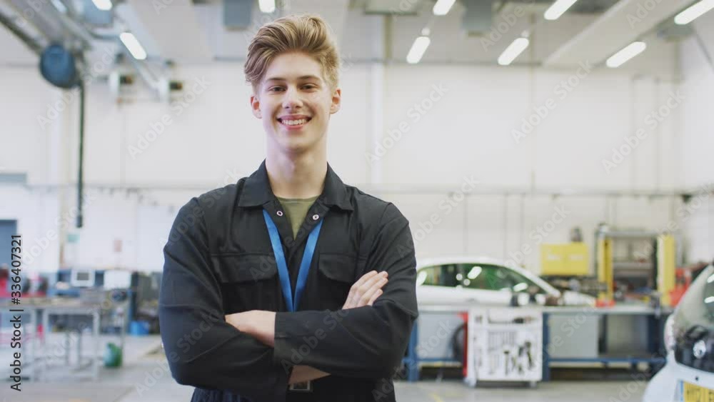 Portrait of male student studying for auto mechanic apprenticeship at college folding arms and smiling at camera - shot in slow motion