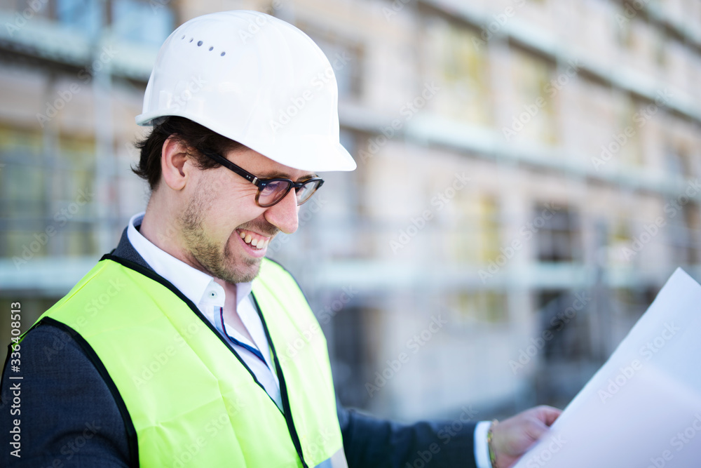 Freudig lächelnder Architekt auf der Baustelle mit Bauplänen Freudig lächelnder Architekt auf der Baustelle mit Bauplänen