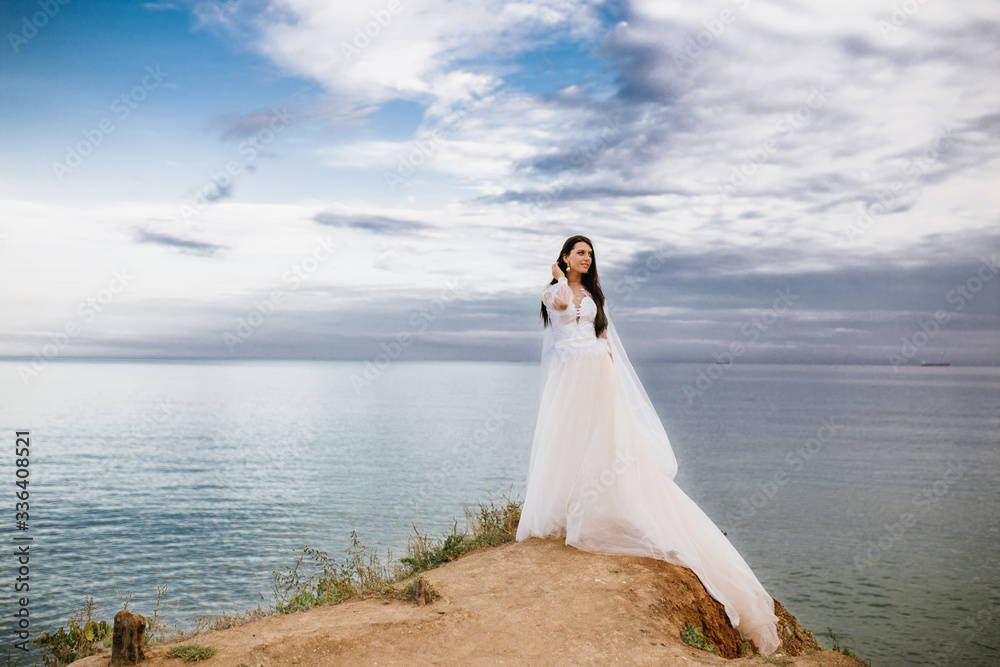 Romantic beautiful bride in white dress posing on terrace with sea and mountains in background Romantic beautiful bride in white dress posing on terrace with sea and mountains in background
