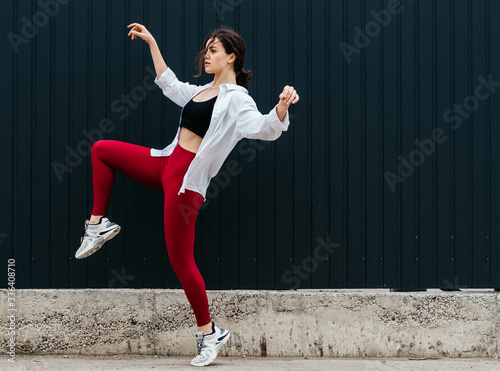 Young female in red leggings and white shirt with one knee up and hands in the air artistic full side view © Cristina