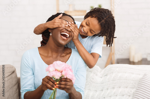 Afro girl congratulating her mom with flowers at home photo