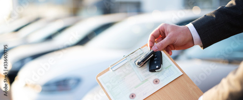 Autokauf, Verkäufer hält Zulassung Papiere und Schlüssel vor einer Reihe an Neuwagen photo