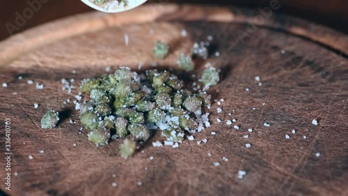 Salt capers on a wooden chopping board, hand moving capers above a wooden cutting board in slow motion, macro and ken burns effect