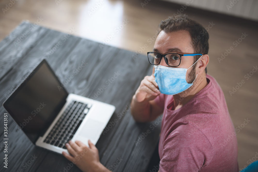 Freelancer with medical protective mask working from home in the days of pandemic and social distancing. Freelancer with medical protective mask working from home in the days of pandemic and social distancing.