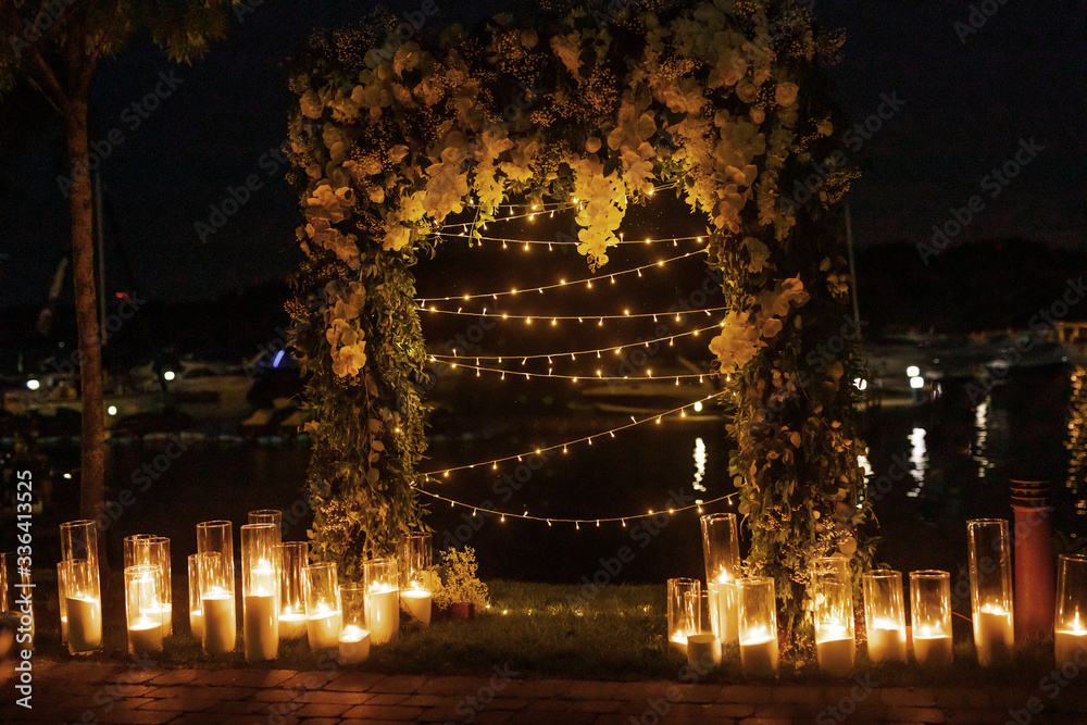 night wedding ceremony, the arch is decorated with flowers, candles and garlands of light bulbs