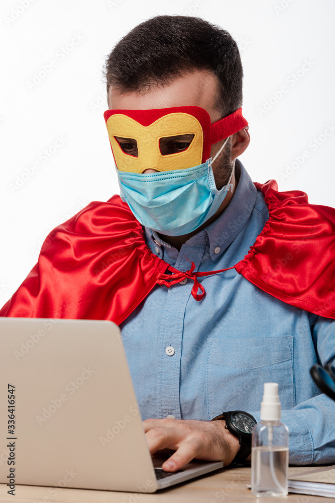 man in medical mask and superhero cape using laptop isolated on white man in medical mask and superhero cape using laptop isolated on white