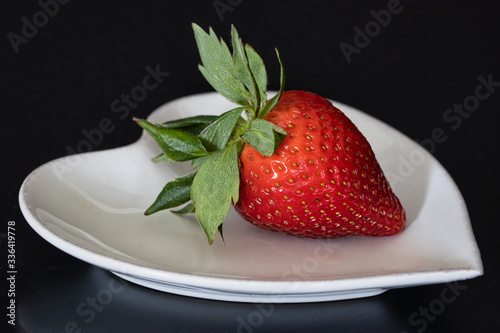 fresh strawberry piece on dark table. Raw juicy strawberry heart shape white plate. black background.