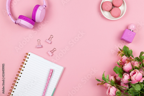 Modern female working space, top view. Women's or girls things, wireless headphones, roses, perfume, stationery on pink backround, copy space, flat lay. Work from home concept. For blog. Horizontal