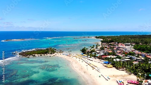 Cinematic aerial of Morro de Sao Paulo blue turquoise beaches, tourists enjoying the beach and sun, and green nature. Bahia, Brazil. Drone slowly moving left photo