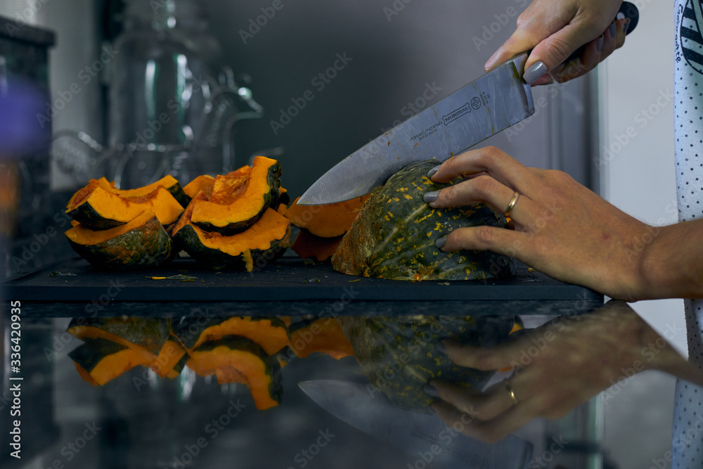 Obraz premium Calabaza siendo cortada por manos femeninas sobre tabla en concina oscura.