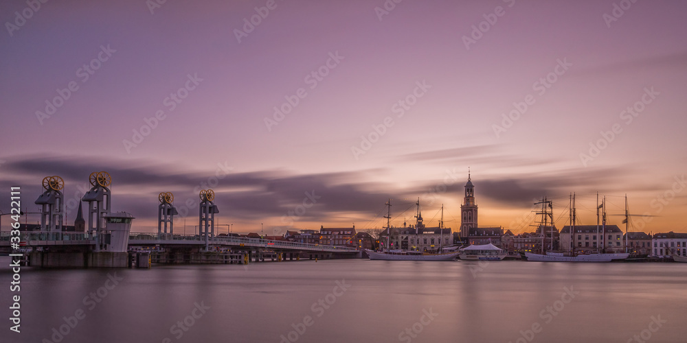 A view on the hanseatic city Kampen, in the Netherlands. Evening skyline photo with Dutch church and towers, its bridge, and some (sailing) ships.
