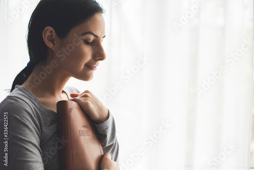 Konstfotografi Portrait of a woman with a surgical mask on her face and a bible held tight to h