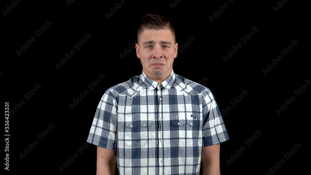 A young man shows an emotion of sadness. Sad man in a shirt on a black background A young man shows an emotion of sadness. Sad man in a shirt on a black background