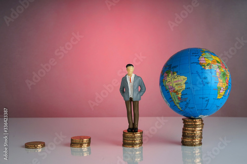 Global capitalism economy lead by successful entrepreneur. Globe, business man maniature on top of stacked coins.  capitalism photo