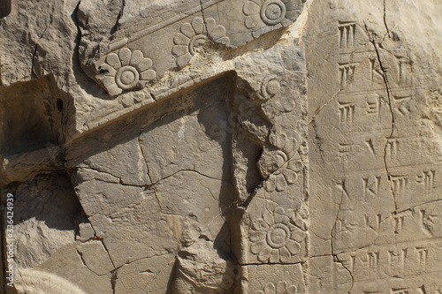 fragment kamiennej rzeźbionej ściany z dekoracjami i pismem klinowym wśród ruin starożytnego miasta persepolis