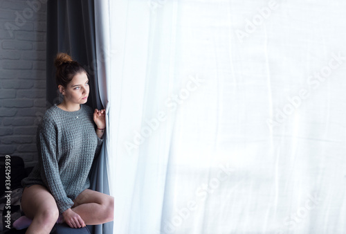 Young woman looking anxiously through a window. Self-isolation 