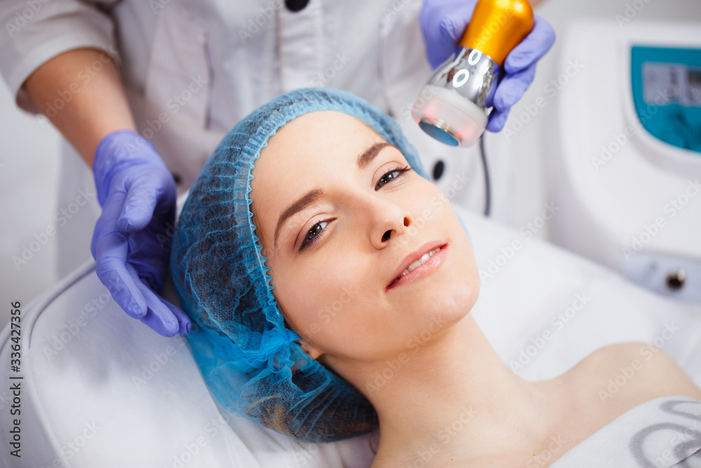 Naklejka premium The procedure of photoepilation in the beauty salon. A young woman is removed unwanted hair on her face. Hardware cosmetology. Close up