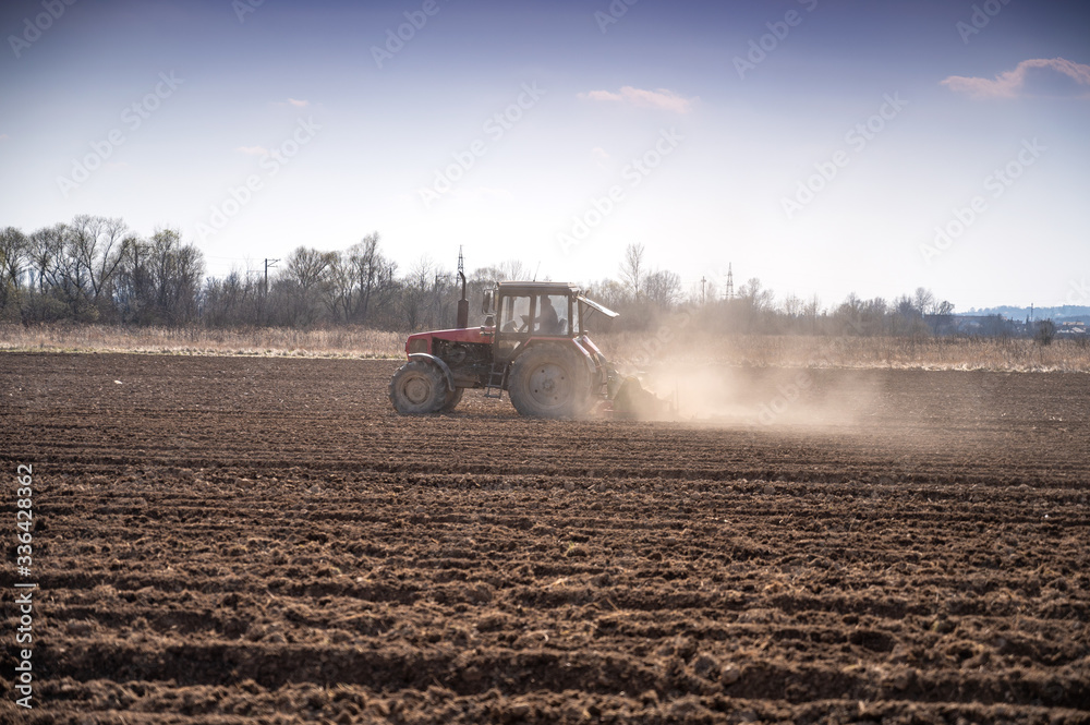 Naklejka premium Farmer in tractor preparing land with seedbed cultivator in early spring