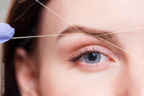 Cosmetologist plucks client eyebrows by thread. Close up