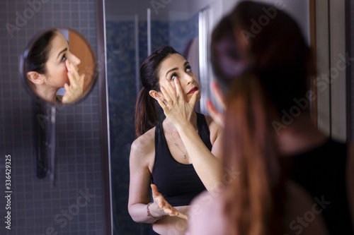  donna si mette il contorno occhi davanti allo specchio nel suo bagno photo