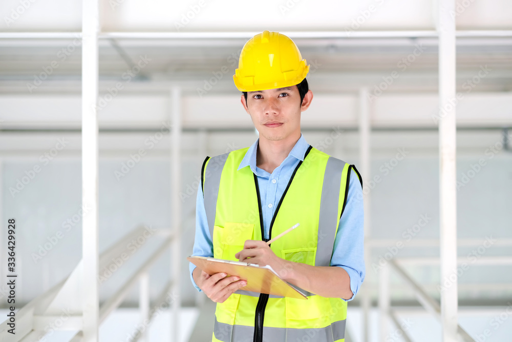 Junior engineer standing in the plant holding the clipboard and pencil with copy space. Wearing safety helmet and safety vest. Feeling happy and smile on work. Engineering and design concept. Junior engineer standing in the plant holding the clipboard and pencil with copy space. Wearing safety helmet and safety vest. Feeling happy and smile on work. Engineering and design concept.