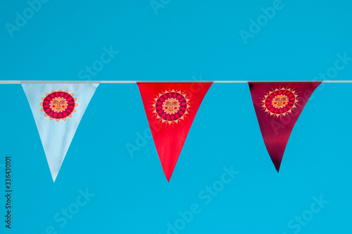 Three triangular flags of different colors with the image of the sun against a blue sky