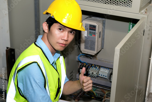 Electrician engineer gave a thumbs up at the control room of plant. Wearing safety vest and yellow helmet. Engineering and control room concept.