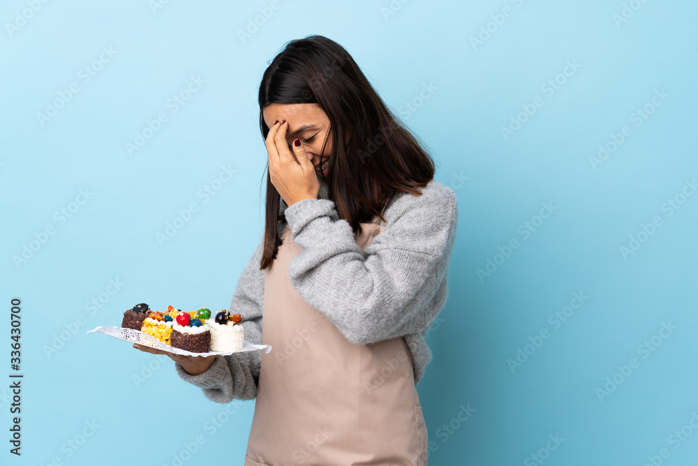 Pastry chef holding a big cake over isolated blue background laughing. Pastry chef holding a big cake over isolated blue background laughing.