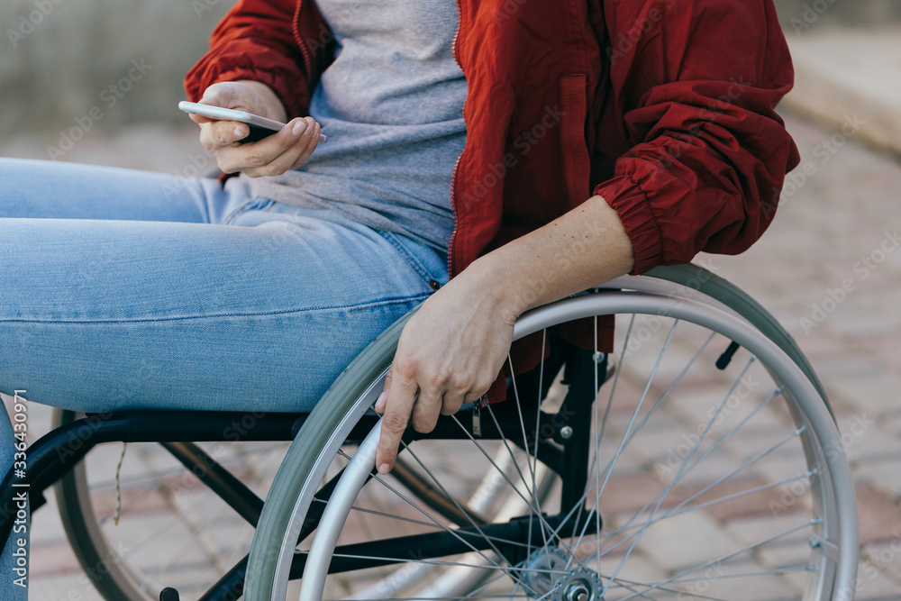 A woman in a wheelchair with a phone in her hand walks on the street, her hand is close up, an unrecognizable man. A woman in a wheelchair with a phone in her hand walks on the street, her hand is close up, an unrecognizable man.