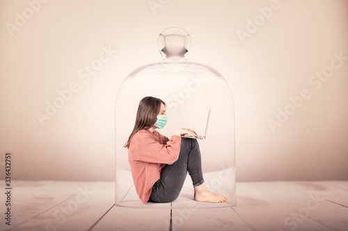young girl with face mask using a laptop in a glass container. Coronavirus continuation concept. photo
