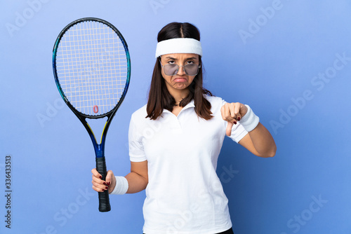 Young woman tennis player over isolated background making good-bad sign. Undecided between yes or not