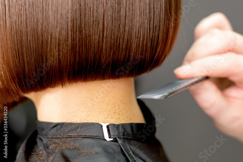 Hairdresser combs short hair of brunette woman close up in hair salon. Toned.