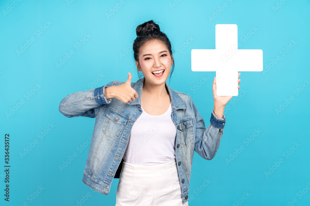 Happiness asian woman smiling, showing plus or add sign and thumb up or like on blue background. Cute asia girl wearing casual jeans shirt and showing join sign for increse and more benefit concept Happiness asian woman smiling, showing plus or add sign and thumb up or like on blue background. Cute asia girl wearing casual jeans shirt and showing join sign for increse and more benefit concept