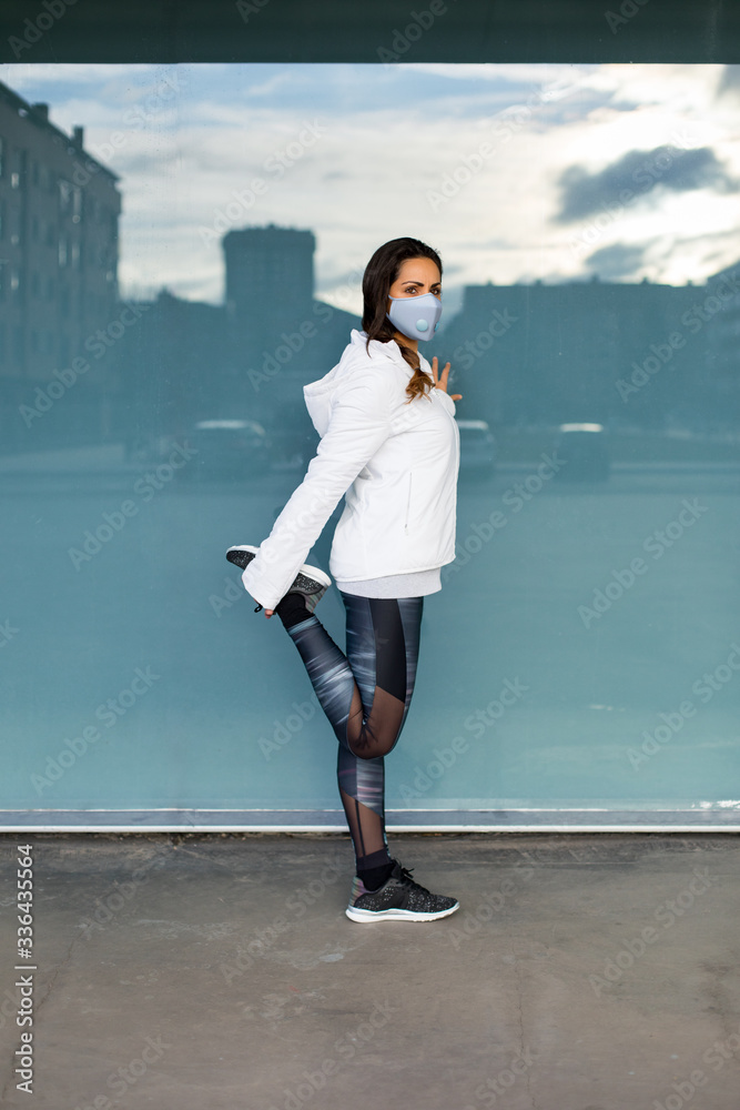 Sporty woman stretching and warming up legs quadriceps before running and fitness urban workout. Healthy fit female athlete exercising outside wearing face mask. Sporty woman stretching and warming up legs quadriceps before running and fitness urban workout. Healthy fit female athlete exercising outside wearing face mask.