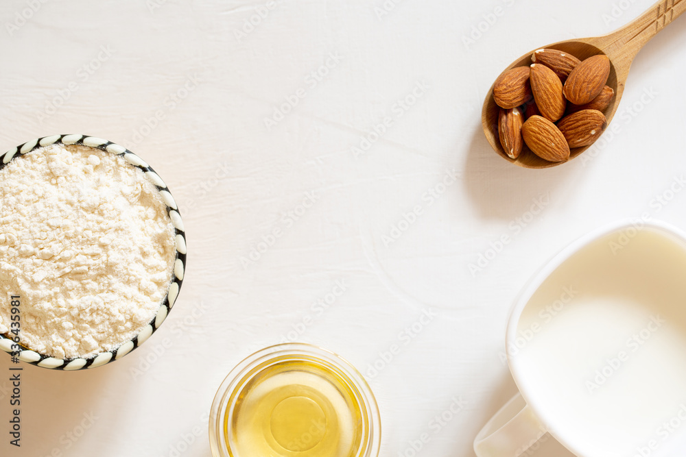 Natural flour, oil and almond seed milk in a glass bowl. Nut almonds in a wooden spoon on a white background. Natural flour, oil and almond seed milk in a glass bowl. Nut almonds in a wooden spoon on a white background.