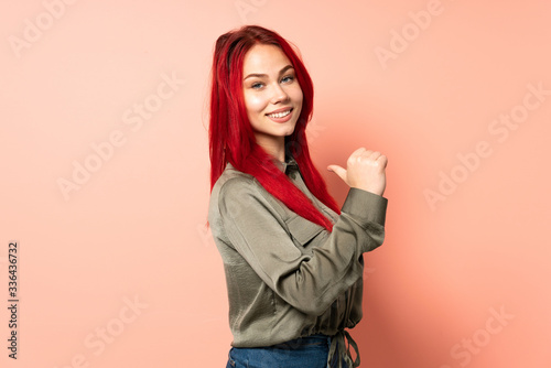 Teenager red hair girl isolated on pink background proud and self-satisfied