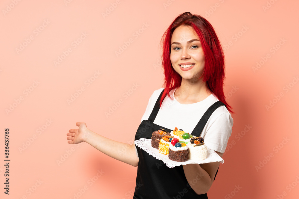 Pastry chef holding a muffins isolated on pink background extending hands to the side for inviting to come