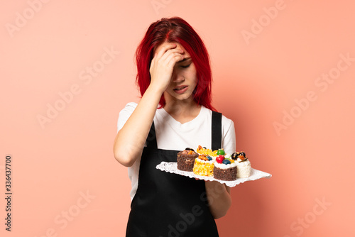 Pastry chef holding a muffins isolated on pink background with headache