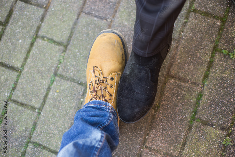 Closeup of two friends making shake with feet in the street to protect against the covid-19 pandemic
