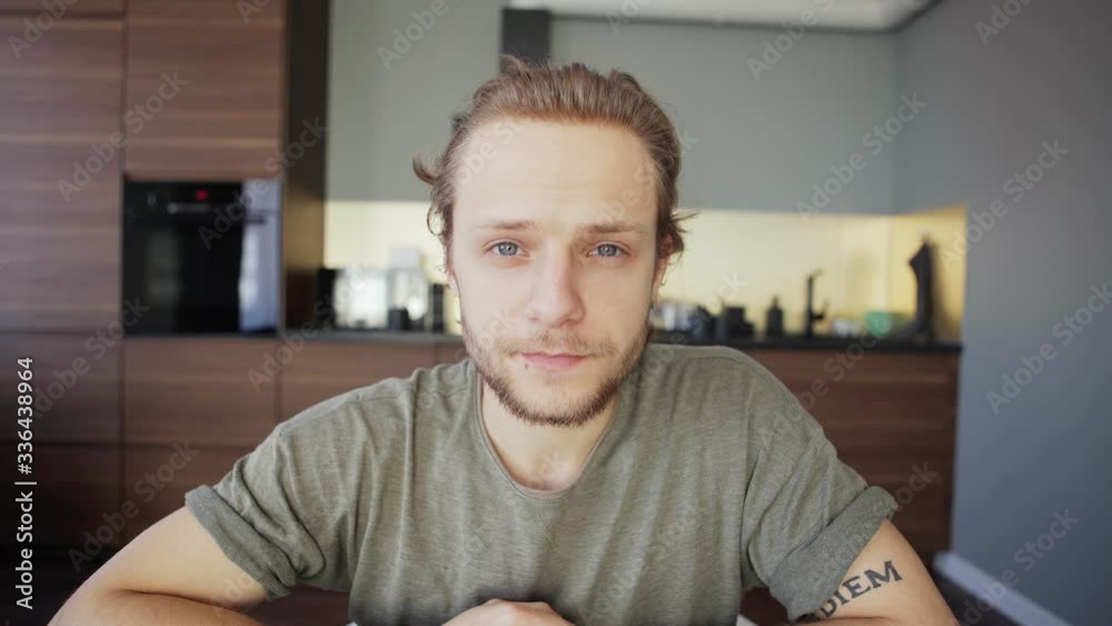 POV tilt up shot of young man working from home and having video conference with colleagues sitting at desk, notepad with sketches and printed templates near him